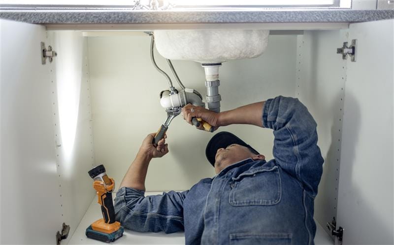 Plumber repairing pipes beneath a bathroom sink in Murrieta