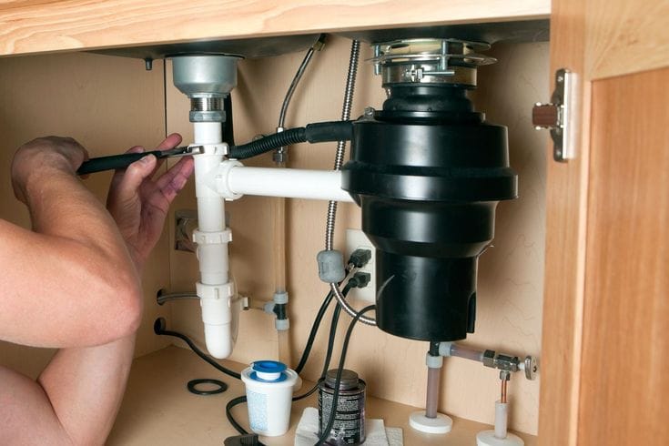 Plumber installing a garbage disposal beneath a kitchen sink in Murrieta