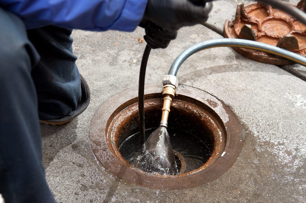 Plumber hydro jetting a sewer line through a manhole in Murrieta