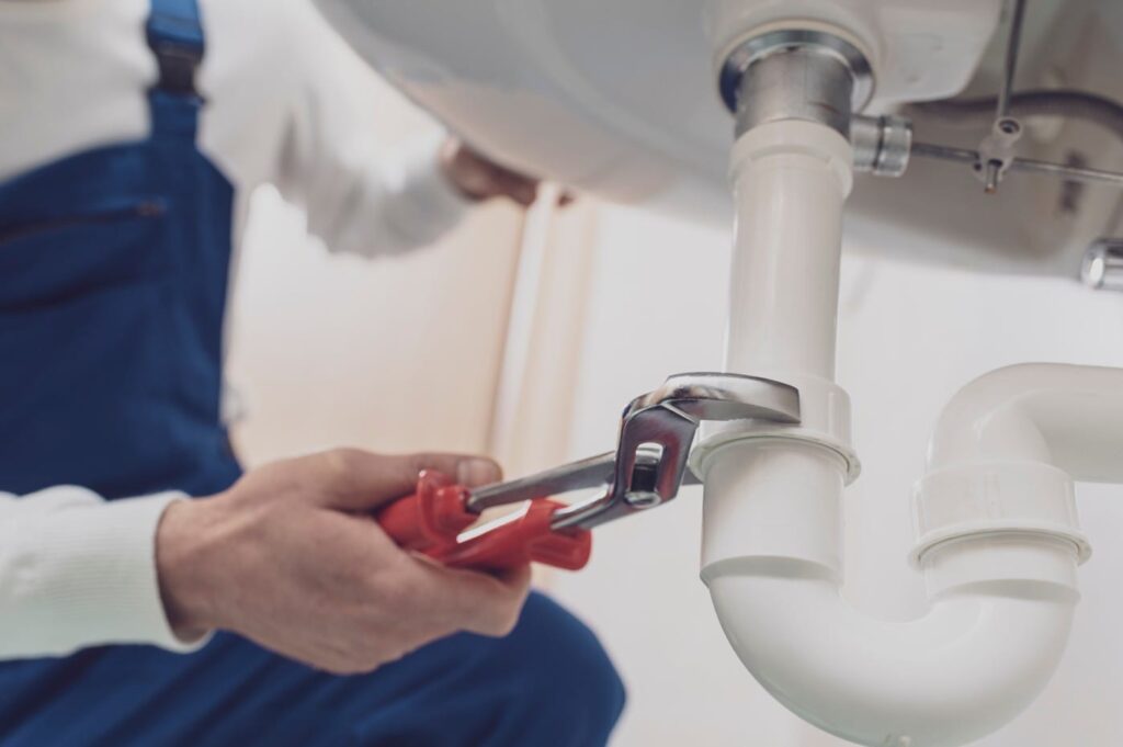 Plumber repairing a white drain pipe beneath a sink in Murrieta