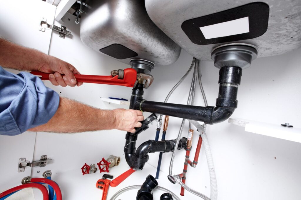 Plumber repairing drain pipes beneath a kitchen sink in Murrieta